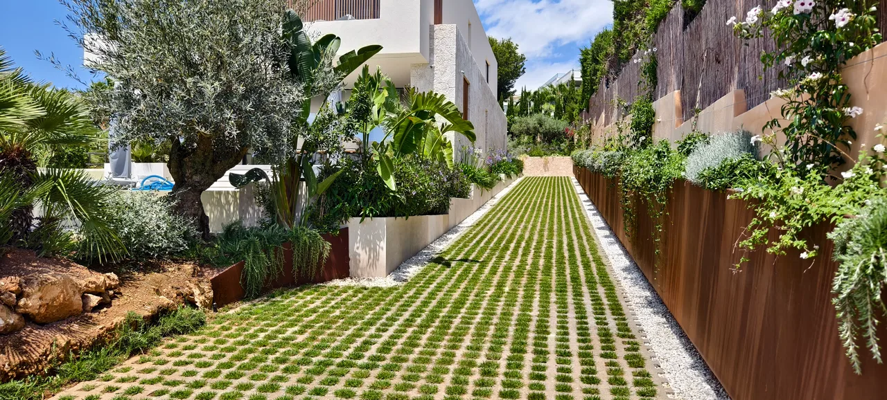 Muro de contención en acero corten sujetando el terreno, con pavimento de césped en el acceso